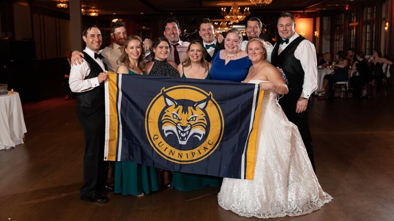 A group of wedding guests hold up a Quinnipiac Bobcats flag
