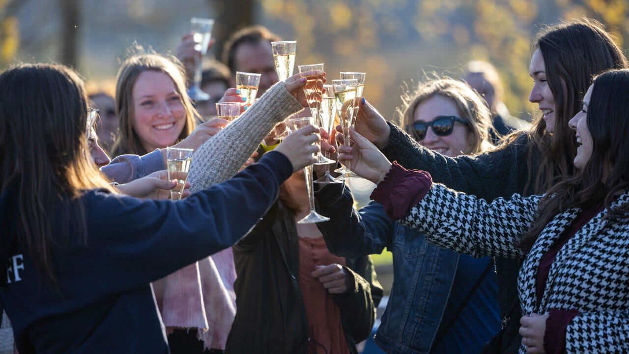 A group of students hold up glasses to toast outside.