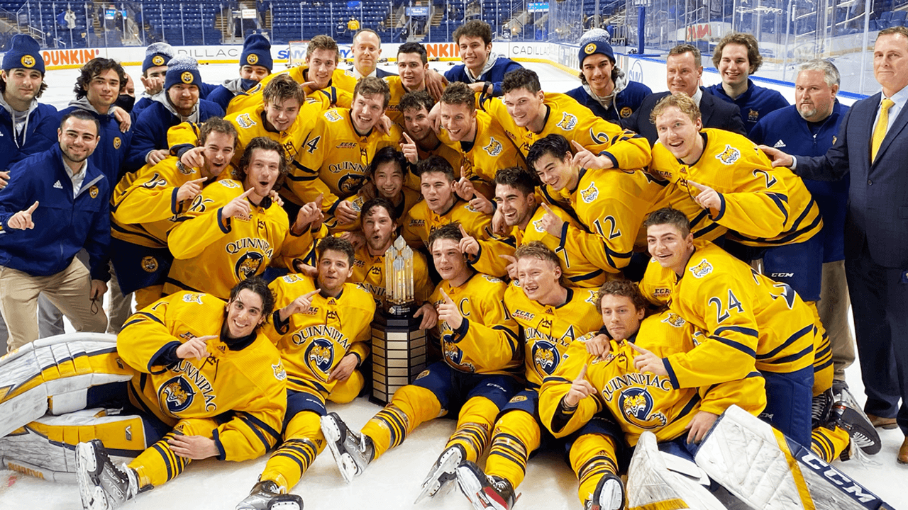 Men's ice hockey team huddles on the ice in celebration with the championship trophy