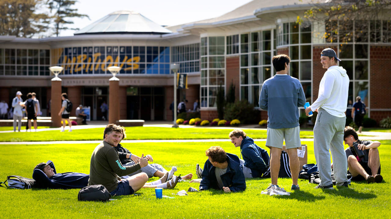 A group of students laughs and sits on the Quad.