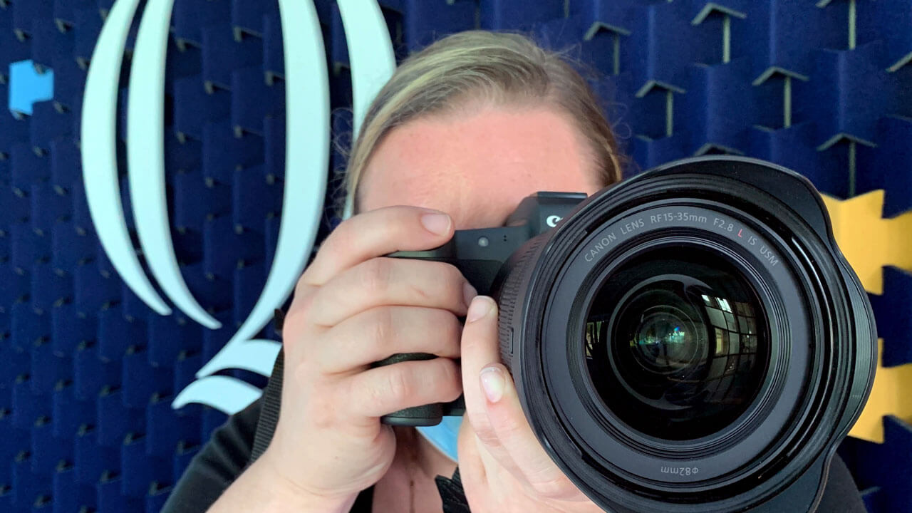 A close up photo of someone aiming a camera for a photo while standing in front of Quinnipiac branding.