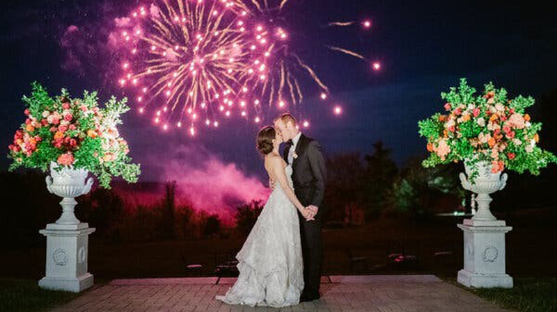 Benjamin Wald and Jacqueline Spar kiss under a sky lit with fireworks on their wedding day