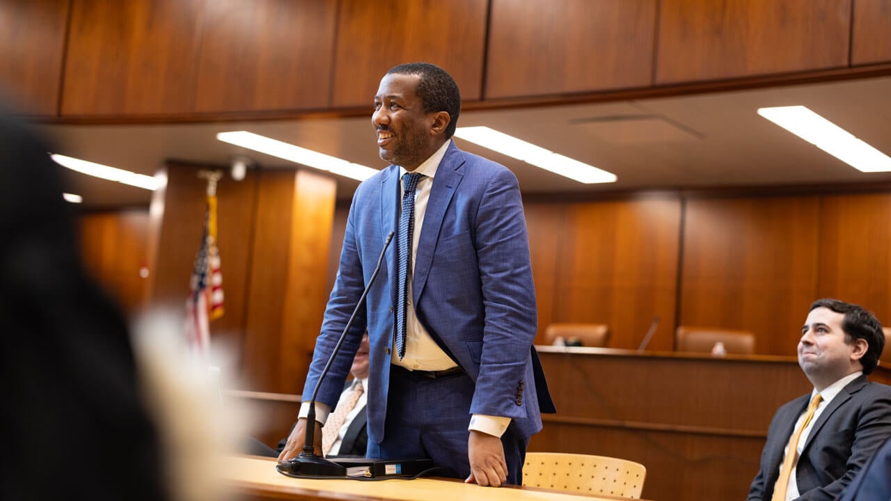 Man in blue suit talking to the crowd of observers in the courtroom