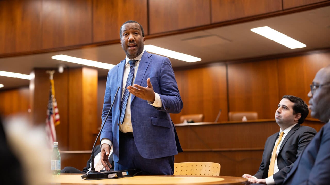 A man in a blue suit addresses a courtroom audience