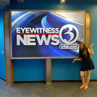 Katie Coen posing in front of a Channel 3 digital sign