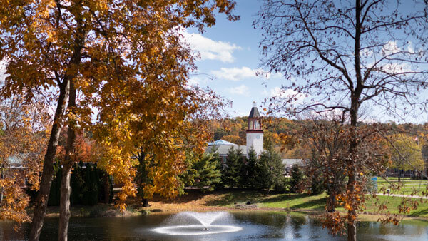 Autumn trees surround the pond with the library clocktower in the distance
