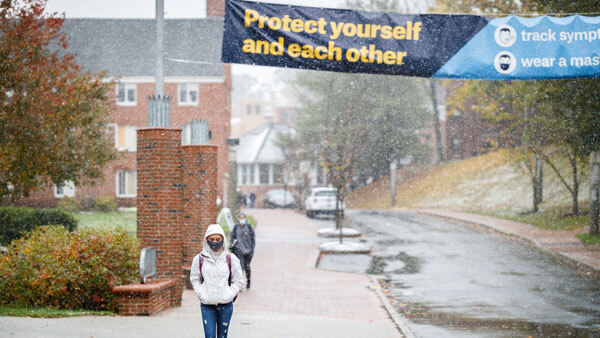 Students walk under signs with reminders of how to stay safe during COVID pandemic