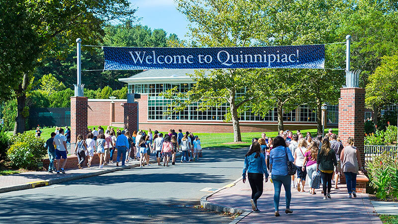 A group of students and their parents walk down Bobcat Way under a "Welcome to Quinnipiac" banner
