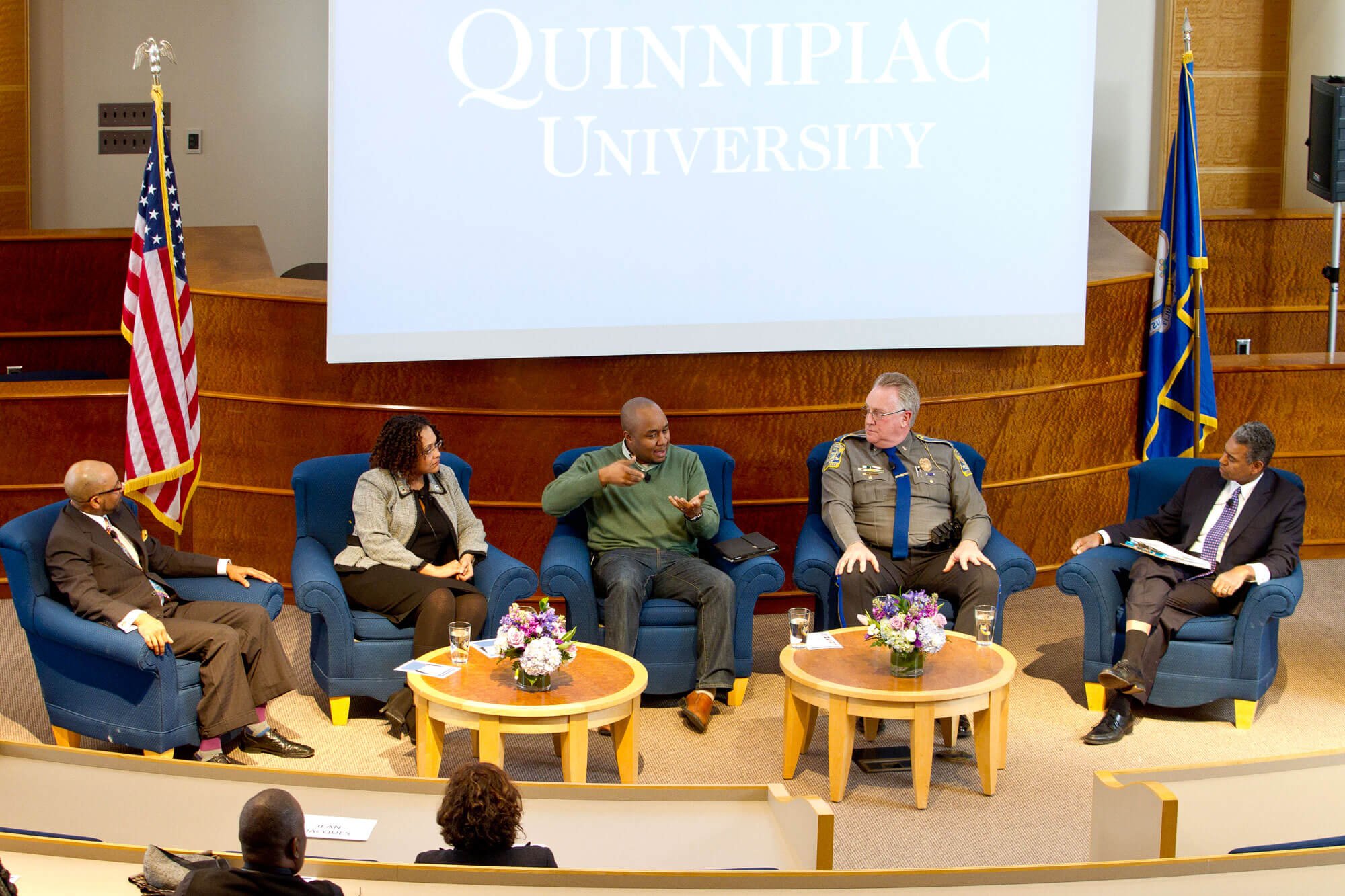 A panel of guests sit at the front of the room in arm chairs having a discussion