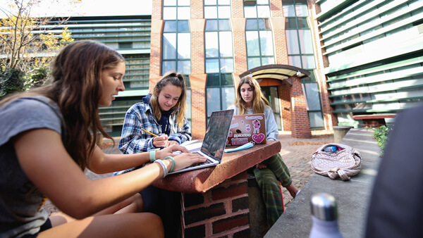 3 students studying together outside at a table