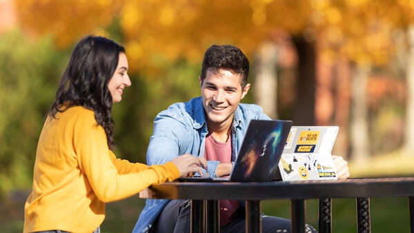 2 students studying together outside at a table