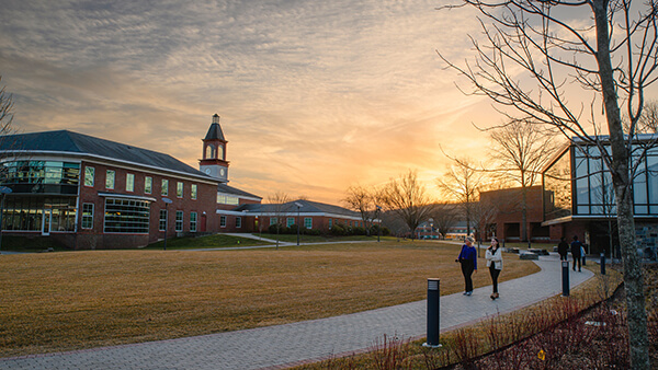 Two people walk by the Recreation and Wellness Center as the sunsets over the clocktower on the Mount Carmel Campus.