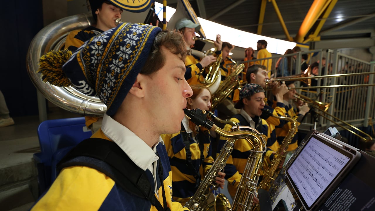 Members of the pep band play their instruments at a hockey game.