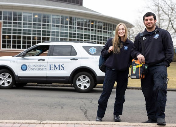 Alex Bayer and Abby Crowell pose in front of QU EMS SUV.