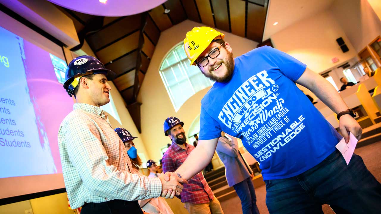 A male student shakes a professor's hand after receiving his hard hat