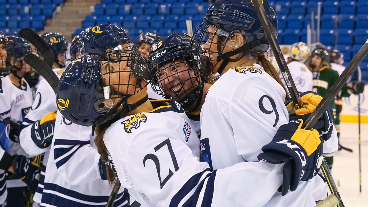 Women's hockey team cheer and hug on the ice after winning a game