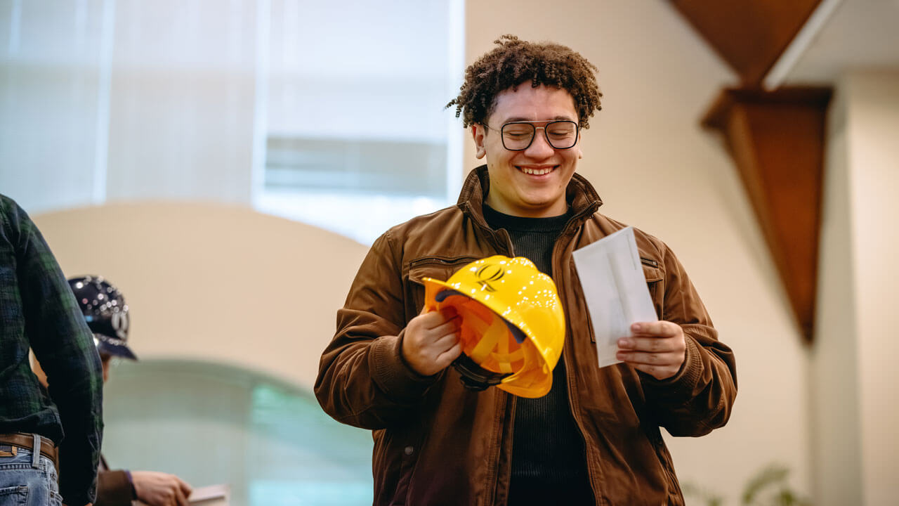 A student holding a hard hat and a paper smiles big.