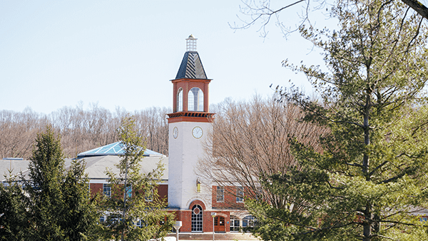 The Arnold Bernhard Library clocktower seen through trees on the Mount Carmel Campus.