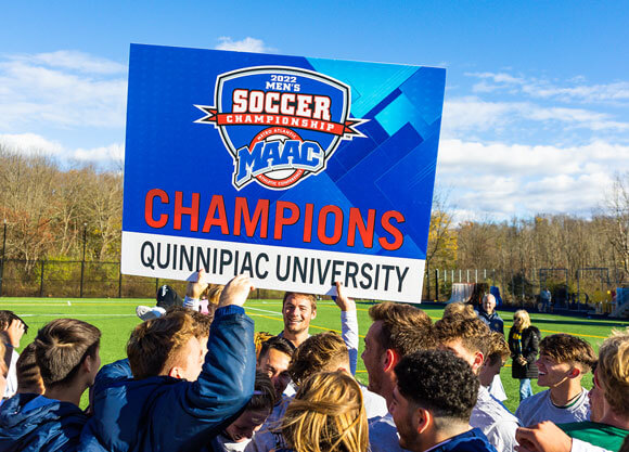 The Quinnipiac soccer team holds up a MAAC Champions sign on the field