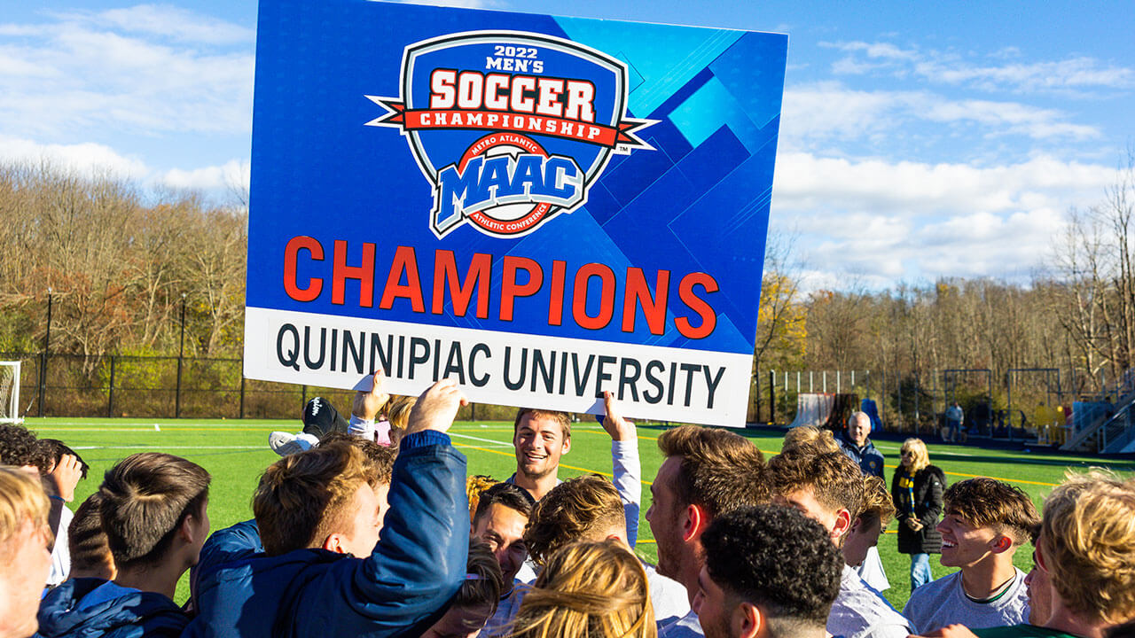 The Quinnipiac soccer team holds up a MAAC Champions sign on the field