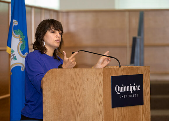 Mónica Guzmán speaks from a podium on the Quinnipiac campus