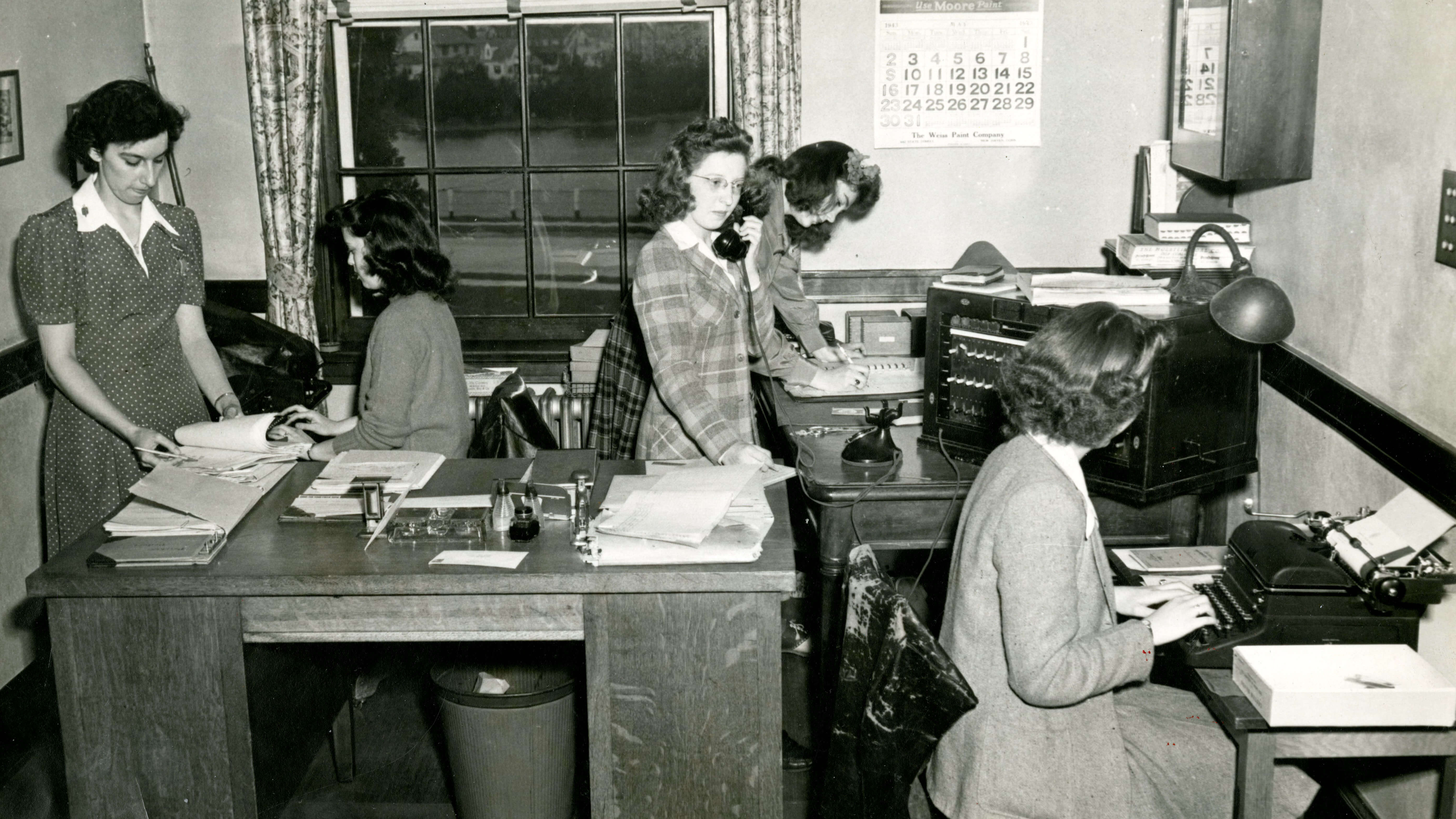 A group of women working at desks with papers and typewriters