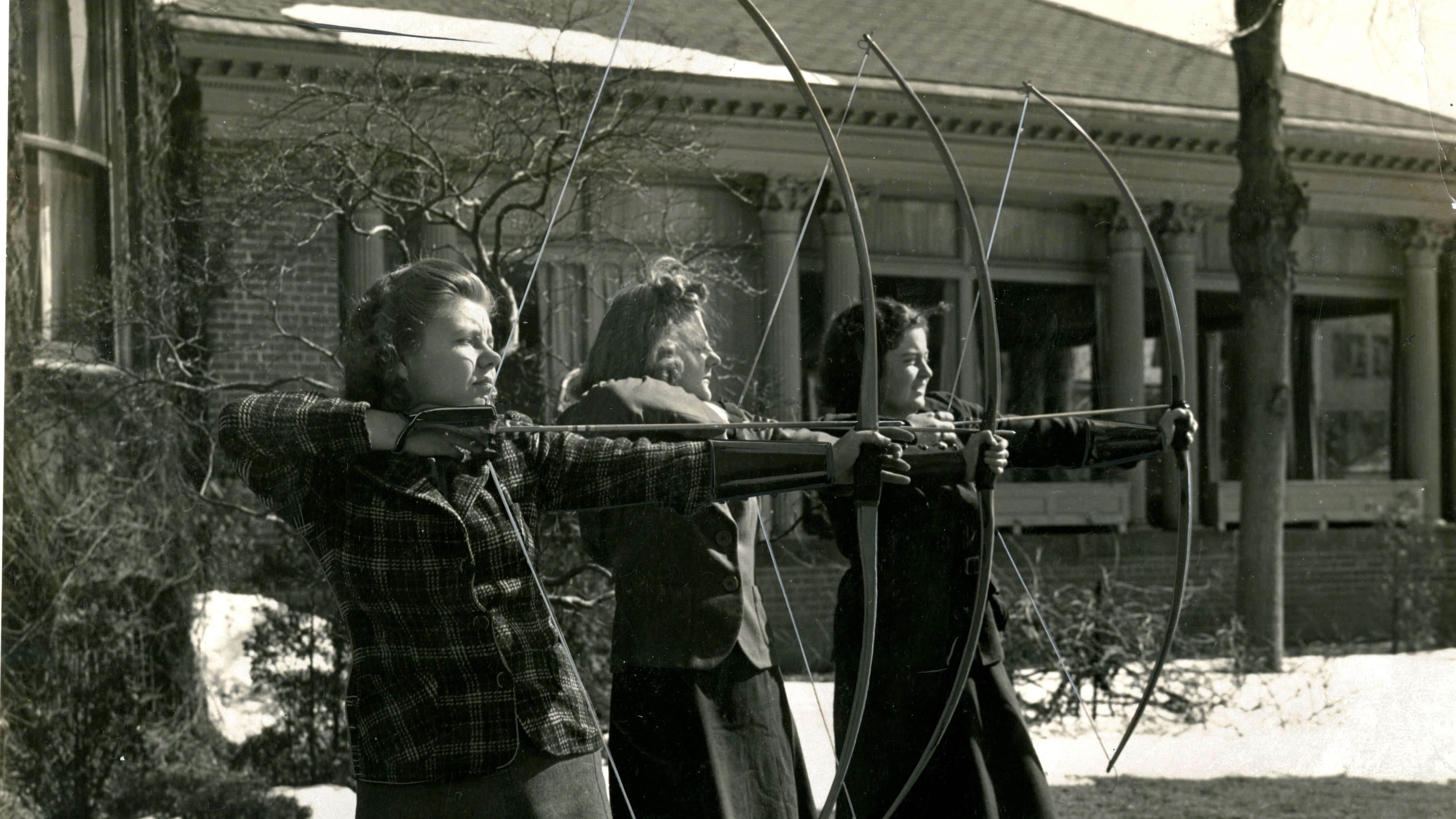 Three women about to release a bow and arrow at the same time