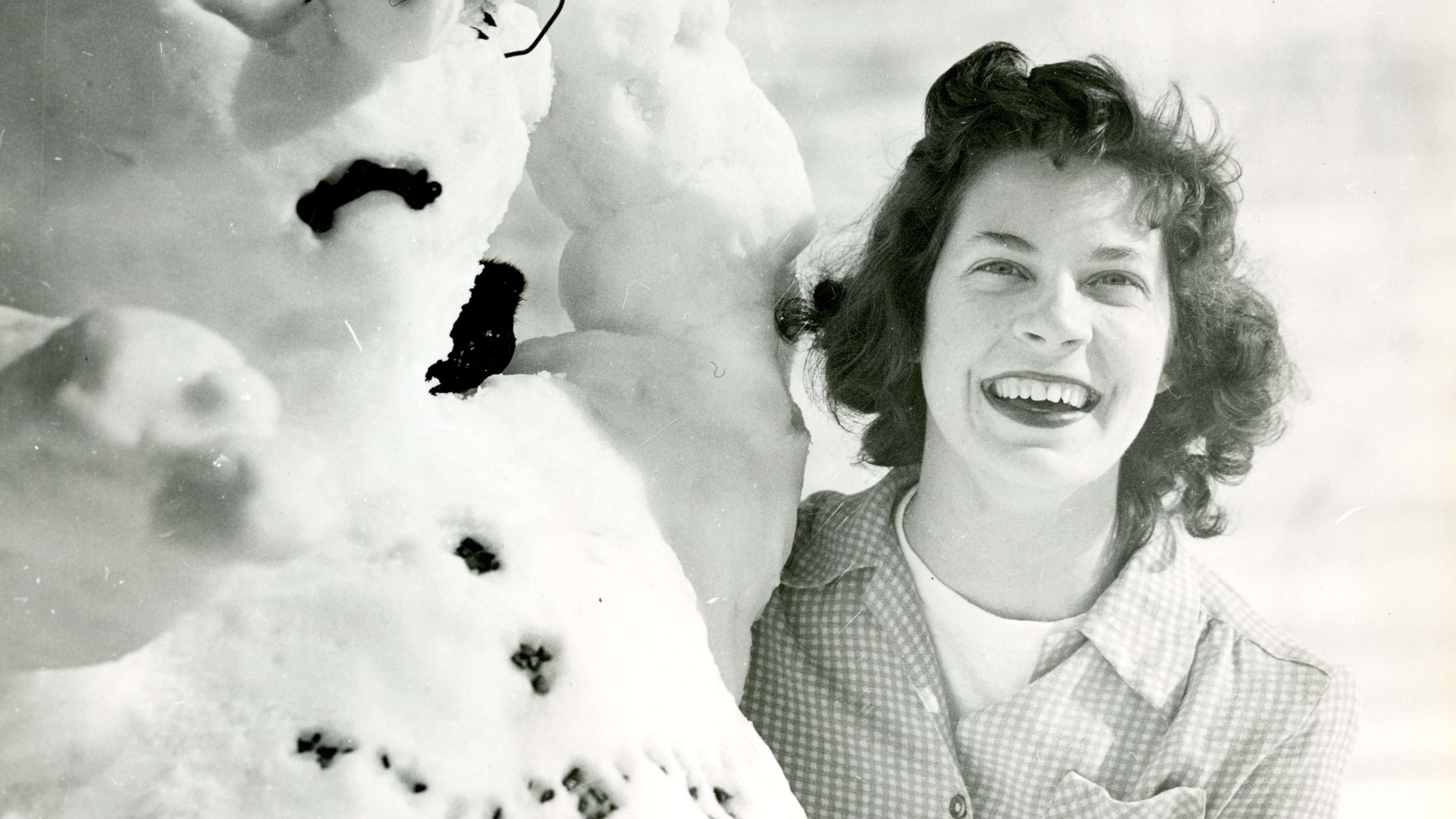 A woman smiles next to a snow man