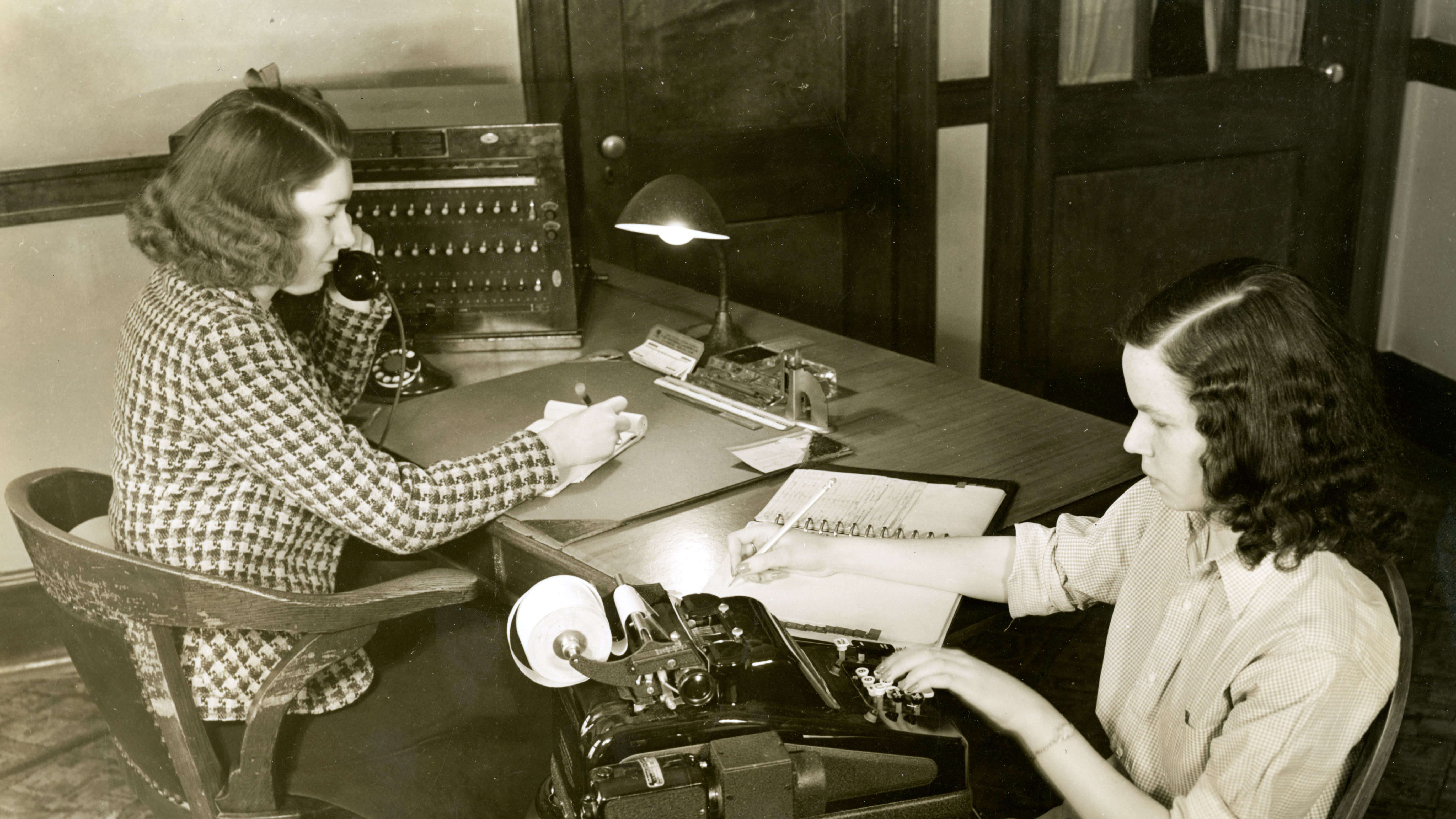 Two women sitting at a desk writing and working