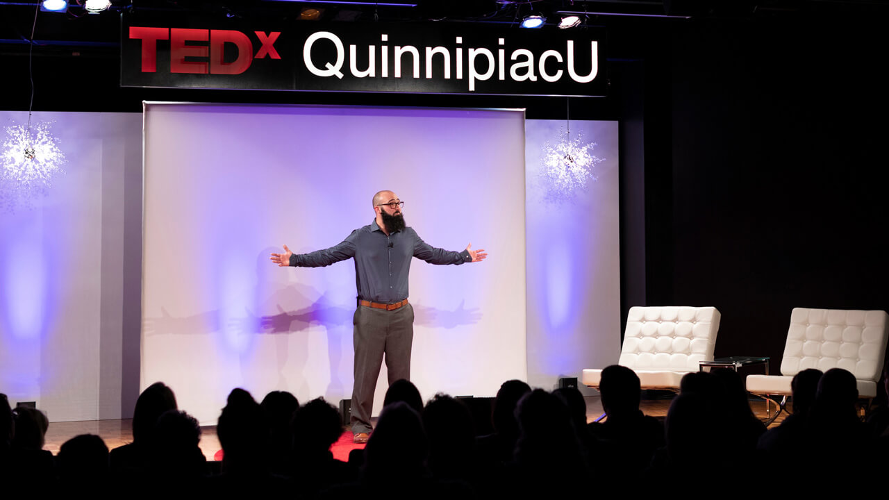 A professor stands on a colorful stage delivery a talk during a TedX event held at Quinnipiac