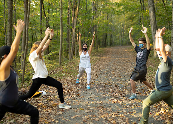 Students perform yoga on a wooded path