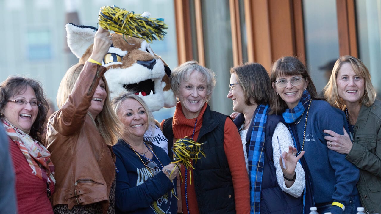 A group of alumni smile and cheer with Boomer the mascot during reunion