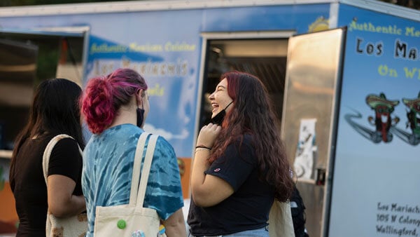 Two students waiting in the food truck line while smiling and chatting
