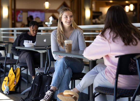 Two students sitting down in Cafe Q with iced coffees from Starbucks