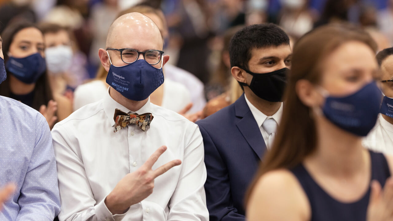 A medical student makes a peace sign as he waits for his match envelope