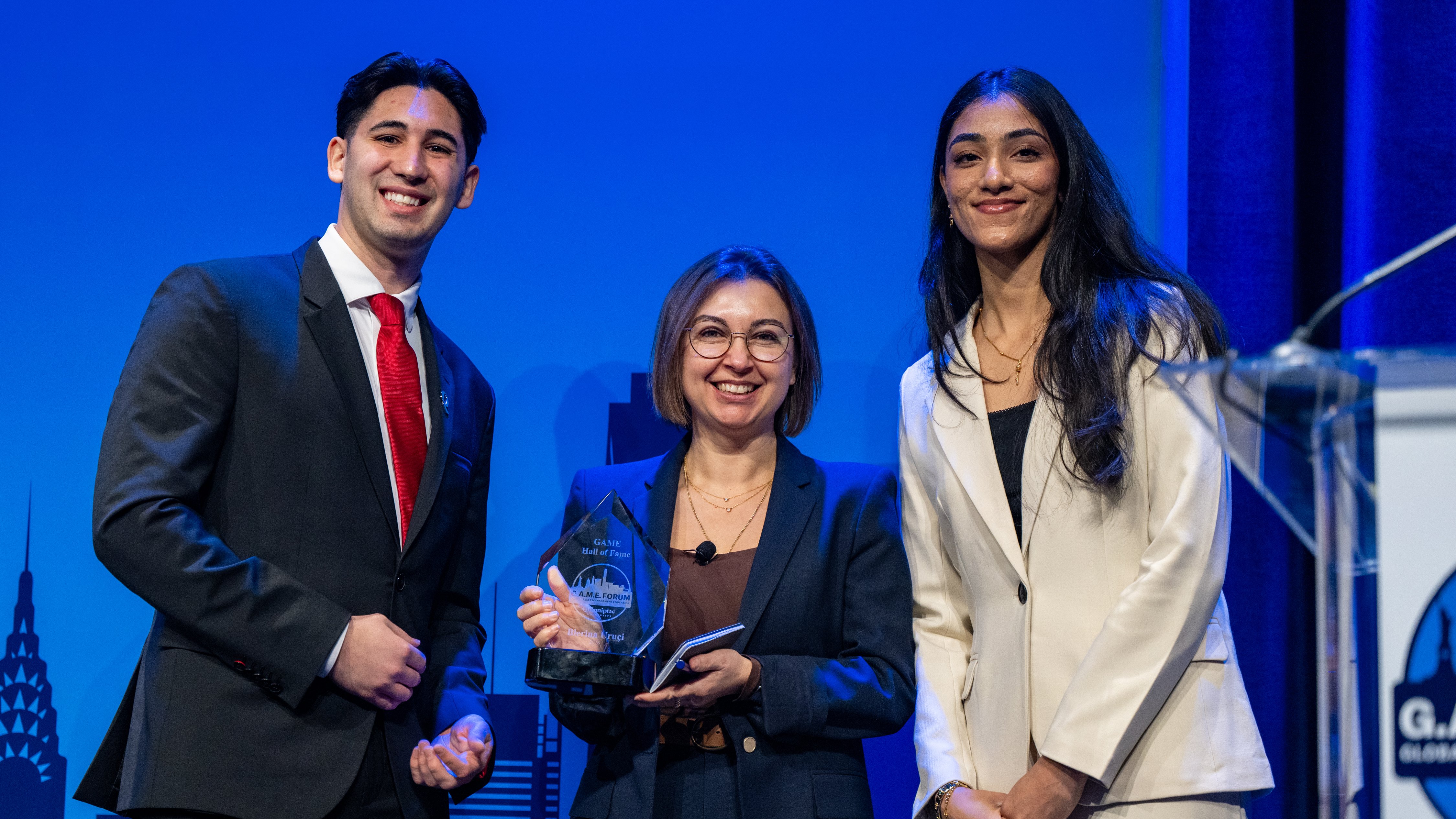 Three people smile with trophy at 15th annual Global Asset Management Education Forum in New York
