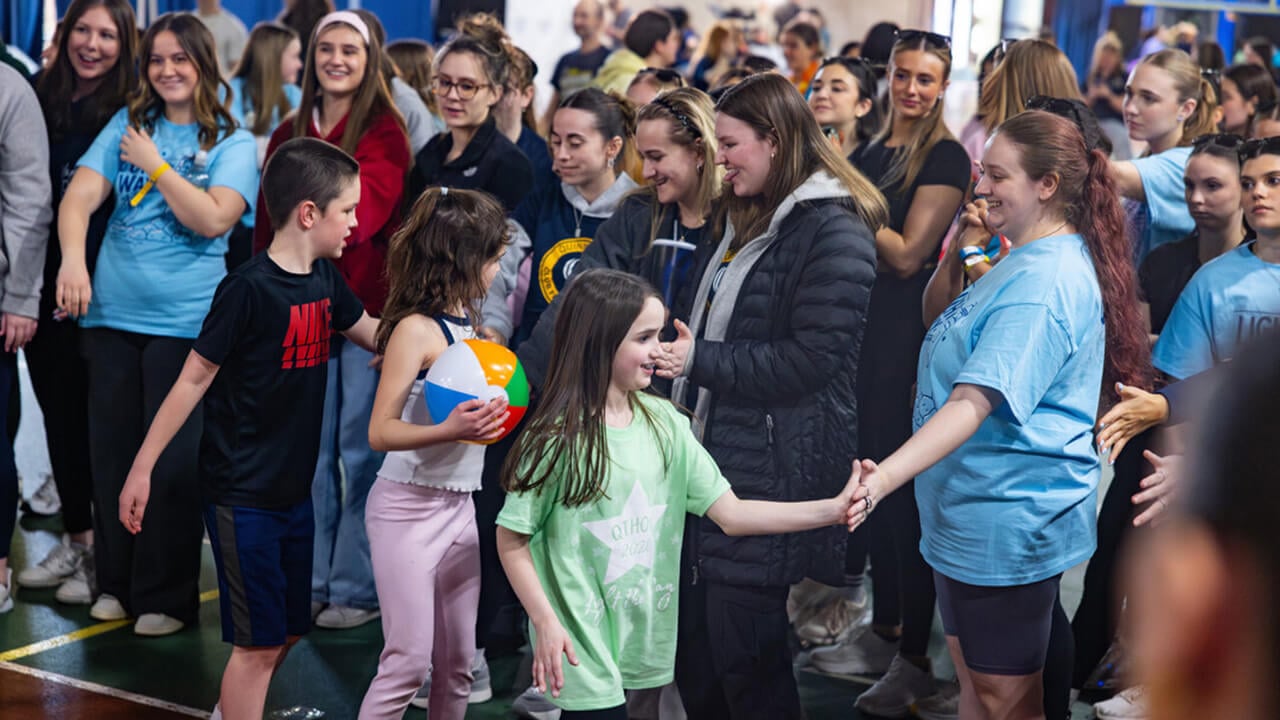 QTHON miracle children go down a line high-fiving students who greet them with smiles and cheers