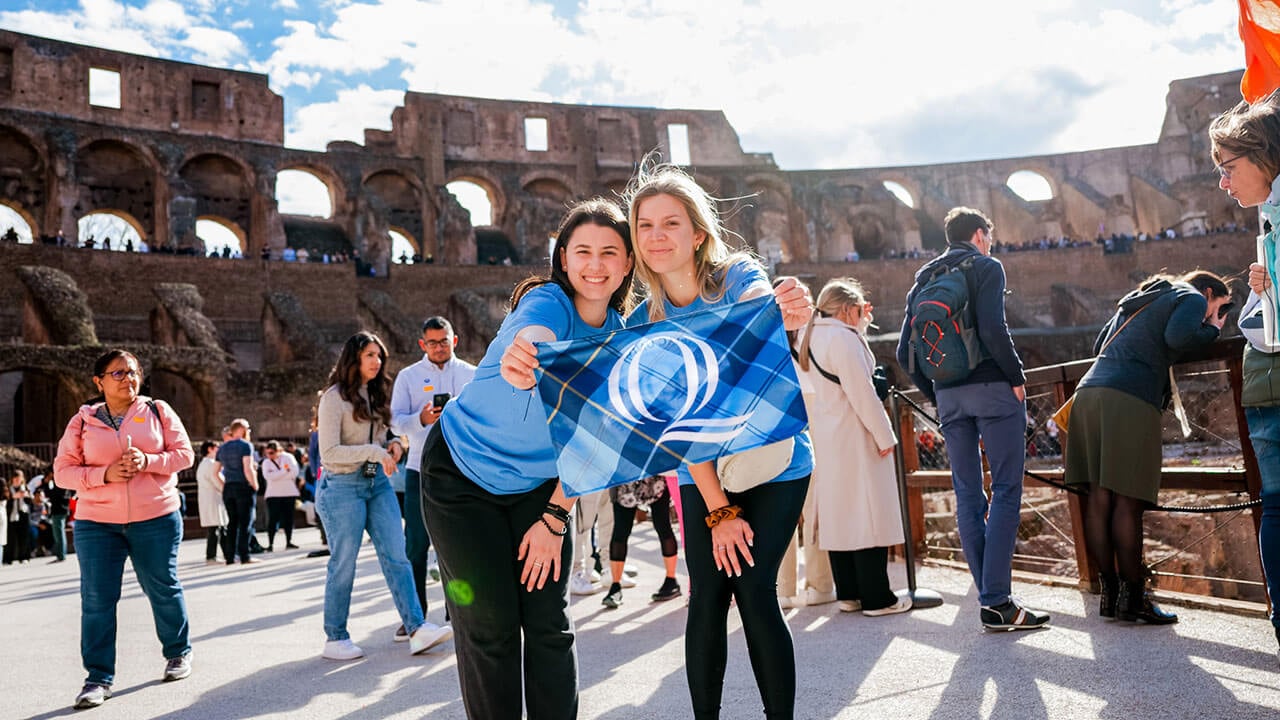 Students take a photo with a Quinnipiac flag at the Colosseum
