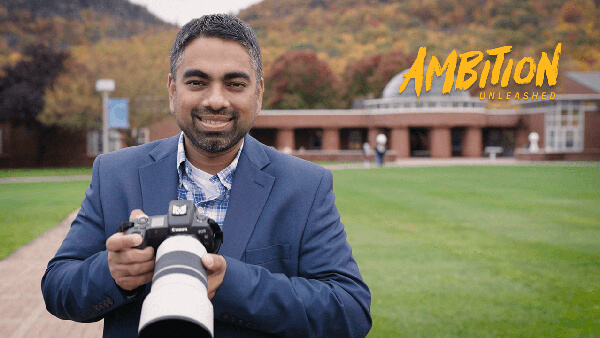Wasim Ahmad stands on the Mount Carmel Campus quad holding a DSLR camera.