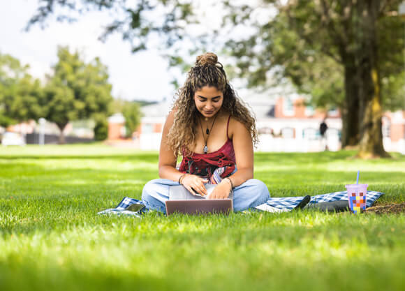 Student working on her laptop outside on the Mount Carmel Campus quad.