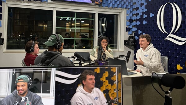 a group of 4 male students sitting around a podcasting table with microphones and headphones