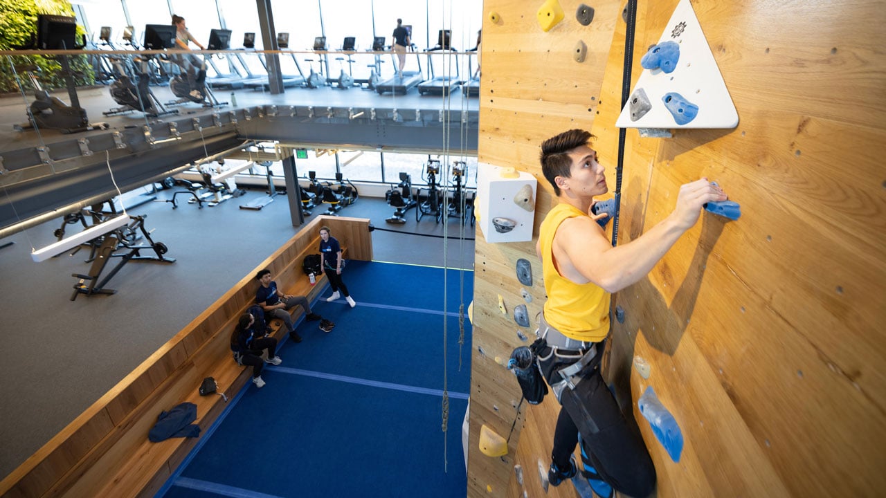 Boy climbing up the rockwall with view of recreation and wellness center