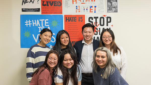 A group of students stand in front of a wall with signs reading "Stop Asian Hate"