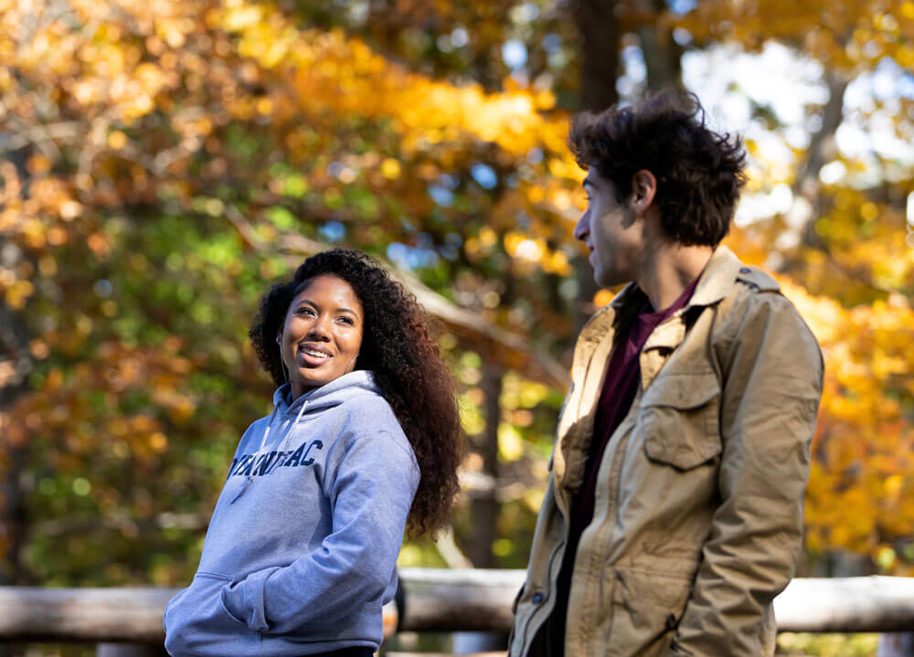 Two students walking together surrounding by fall foliage.