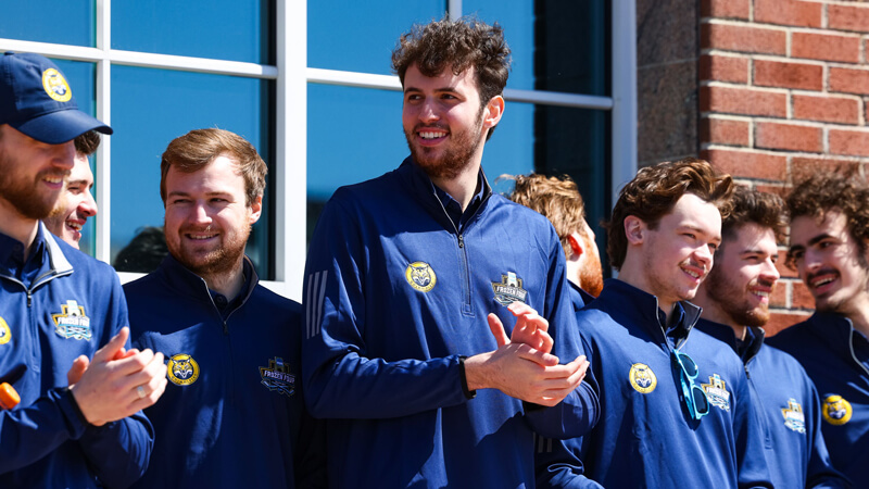 Men's ice hockey team members clap in the sunshine on the library steps