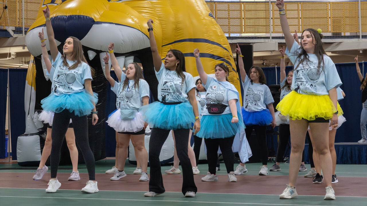 Several students in matching shirts dance in front of an inflated bobcat during QTHON