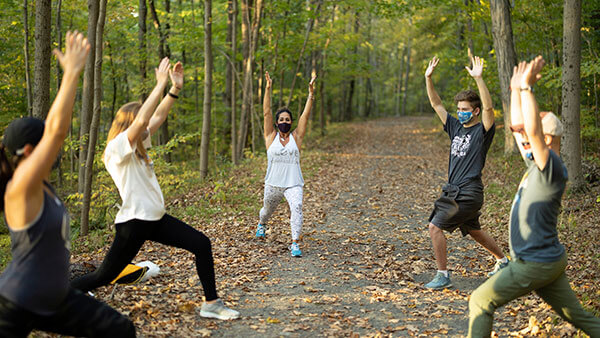 Tami Reilly leads students in performing yoga on a wooded path