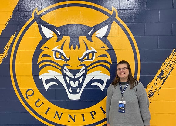 Madison Tornberg '27 standing in front of the Quinnipiac Logo