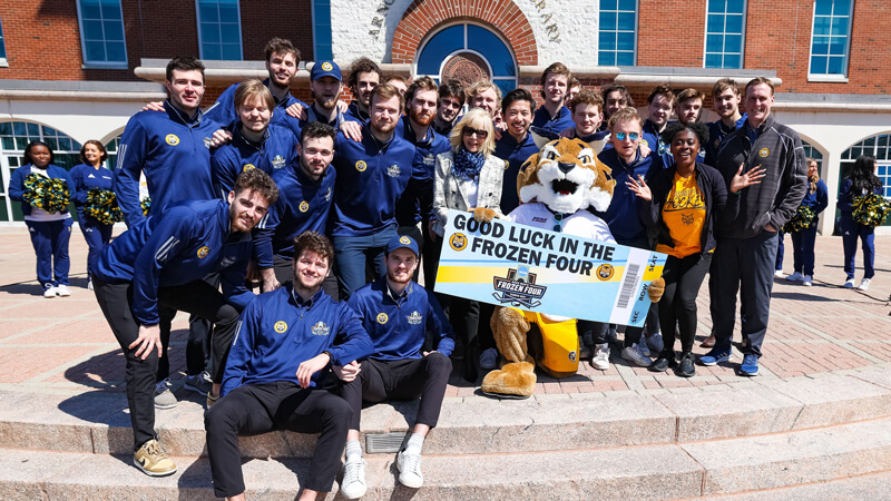 President Olian and the men's ice hockey team smiles with Boomer and an oversized Frozen Four ticket