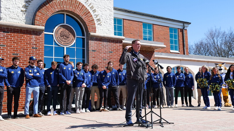 Men's ice hockey team Head Coach Rand Pecknold speaks to the crowd from the library steps